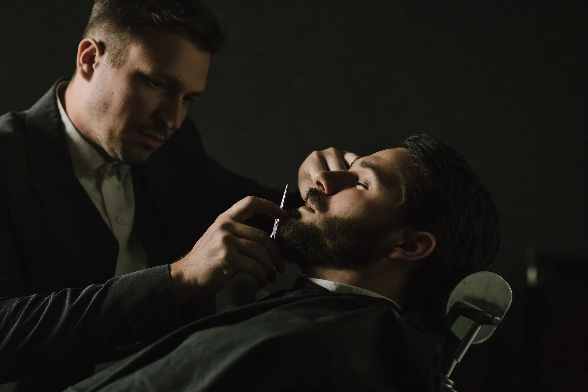 Le barbier taille la barbe d'un client dans une lumière tamisée