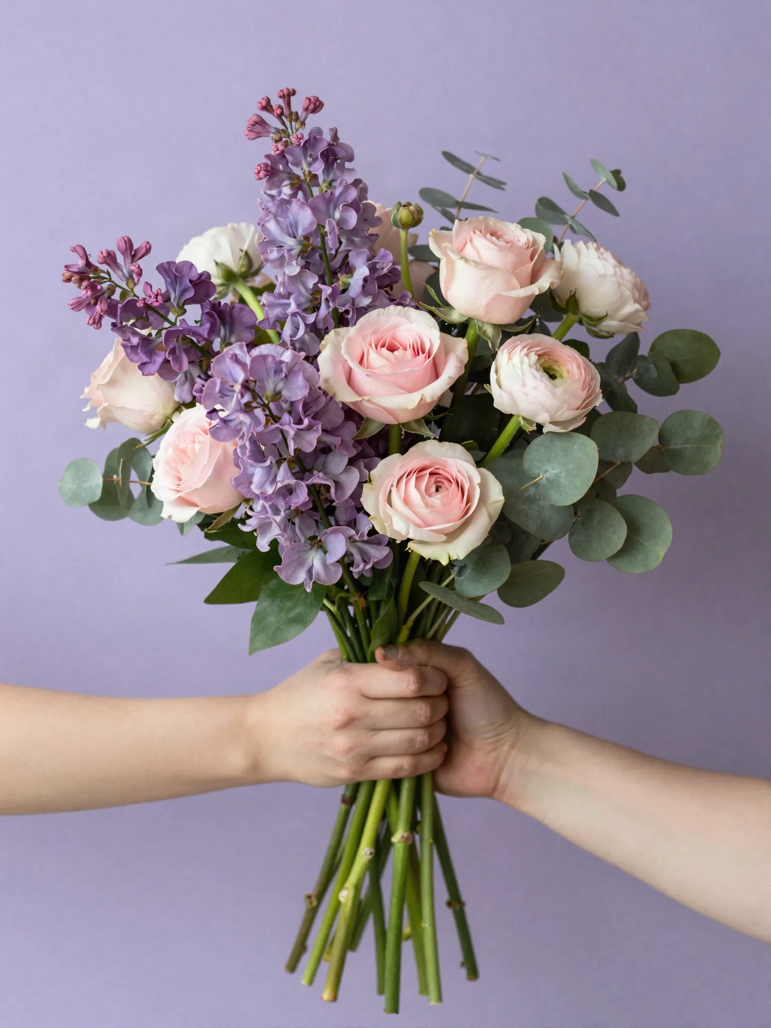 Bouquet de pois de senteur lilas, roses et renoncules tenu devant un mur lilas
