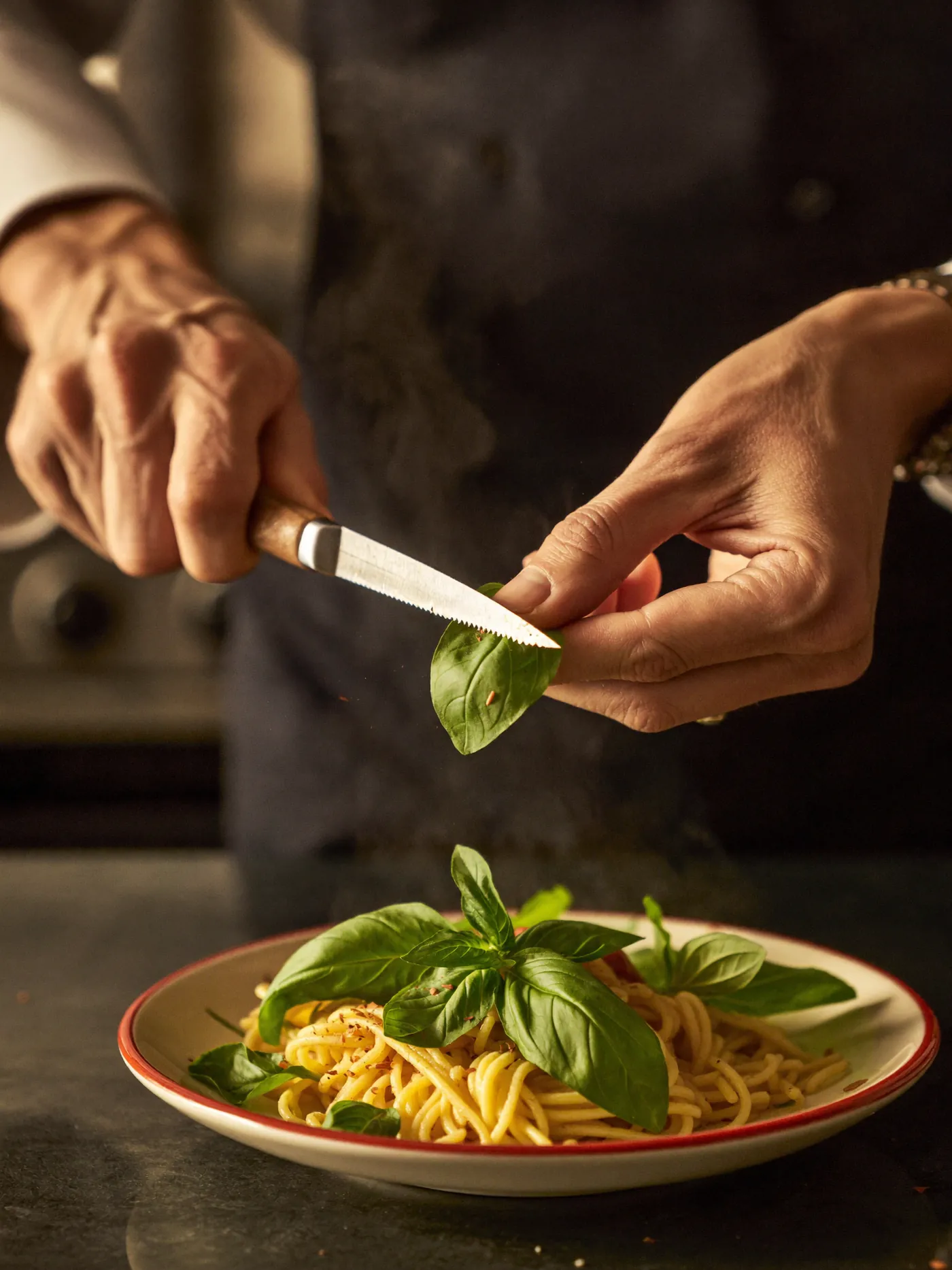 Le chef dépose du basilic frais sur une assiette de pâtes