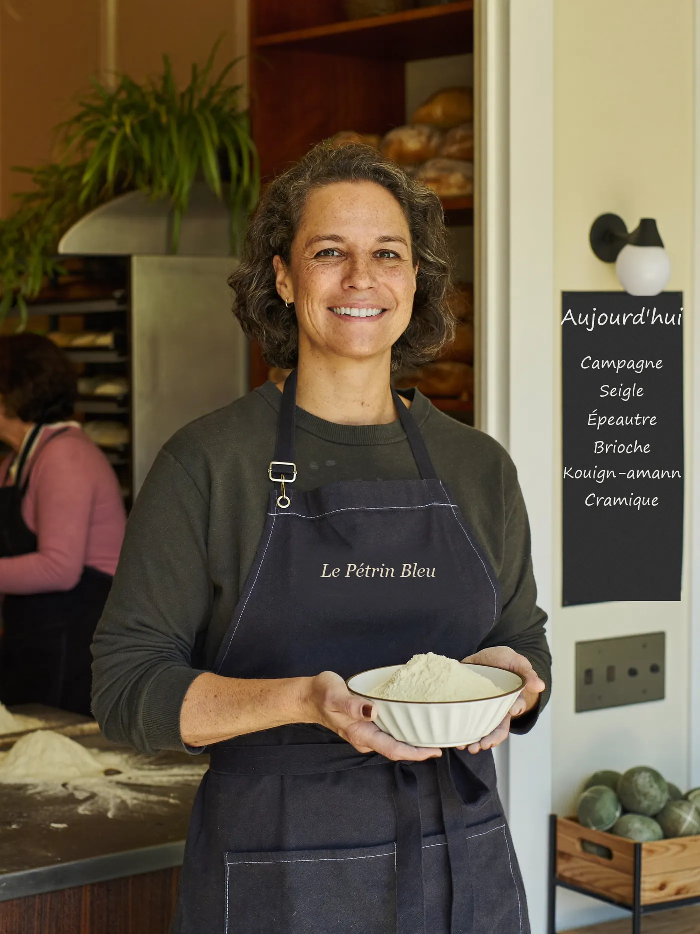 Élise, la boulangère, souriante dans sa boutique avec un bol de farine